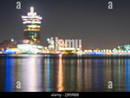Skyline sfocato di Amsterdam di notte, luci sfocate del traffico e edifici moderni intorno al fiume IJ nelle vicinanze della stazione centrale Foto Stock