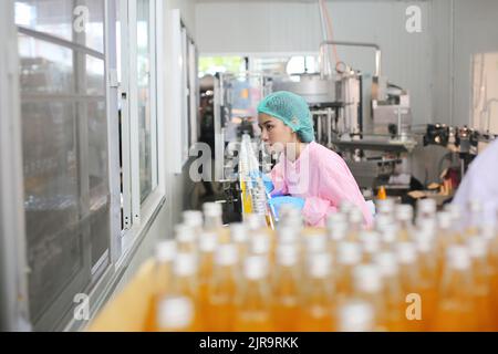 lavoratore che controlla il lavoro della macchina nella linea di produzione dell'industria delle bevande. Foto Stock