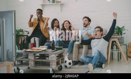 Gruppo di amici felici guardando gioco di sport in TV a casa al coperto. Sono felici della loro squadra preferita vincere la concorrenza Foto Stock