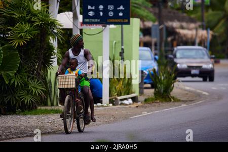 Un uomo locale in bicicletta con il bambino su una strada alla luce del giorno a Puerto Viejo, Costa Rica Foto Stock