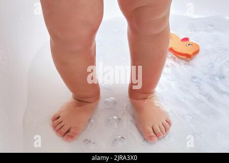 Le gambe dei bambini sono in piedi su un tappetino antiscivolo nella vasca da bagno. I piedi del bambino si lavano sul tappeto antiscivolo in bagno. Bambino di un anno Foto Stock