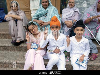 Sui gradini del Centro Culturale Sikh, i bambini che mangiano fanno un segno di pace seduti davanti agli anziani. A Richmond Hill, Queens, New York. Foto Stock