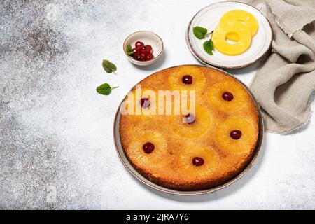 Tradizionale torta di ananas fresco al forno capovolto con ciliegie glace su uno sfondo rustico chiaro. Delizioso concetto di cibo dolce fatto in casa. Foto Stock