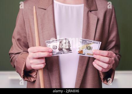 Insegnante di donna che tiene conto del dollaro strappato sulla lavagna della scuola in classe Foto Stock