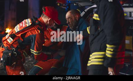 I lavoratori del servizio di emergenza multirazziale che mettono coperta e bandito la mano ferita dell'uomo anziano durante l'interrogazione dopo l'incidente di notte Foto Stock