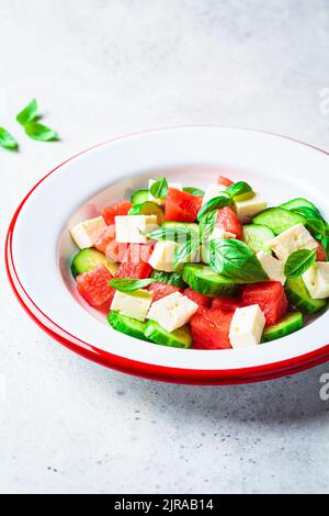 Insalata di cocomero con feta, cetriolo e basilico in un piatto, fondo grigio. Ricetta estiva, dieta sana, cibo disintossicante. Foto Stock