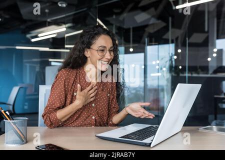 Donna d'affari ispanica felice che lavora in un ufficio moderno utilizzando un computer portatile per videochiamare e riunioni online con colleghi dipendenti, donna sorridente e divertente dando una presentazione Foto Stock