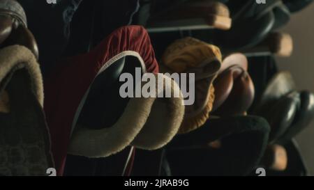 Varie selle a cavallo appese sulla cremagliera sul muro di stalla fioca in fattoria Foto Stock