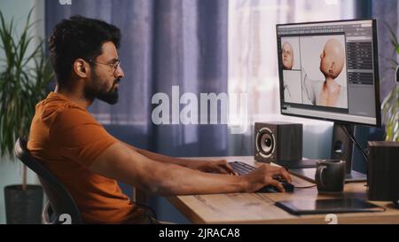 Vista posteriore di un uomo anonimo che crea un modello 3D di personaggio videoludico seduto al tavolo e lavorando a un progetto remoto a casa Foto Stock