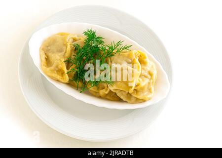 Gnocchi asiatici fritti Gyozas o gnocchi russi, ucraini, cerotti in piatto di ceramica bianca servito con panna acida. Primo piano. Cena asiatica. Giacitura piatta. Sfondo isolato bianco. Copia spazio. Foto Stock