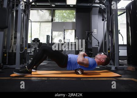 Scatto completo di un uomo di fitness che si rilassa dopo l'allenamento, usando il rullo di schiuma sui muscoli della schiena Foto Stock