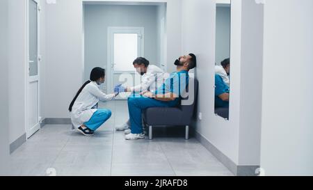 Medico femminile che cammina nel corridoio e si unisce agli uomini poi cominciando a parlare e sostenere i colleghi durante la pausa in ospedale moderno Foto Stock