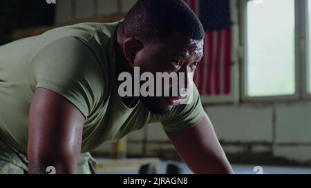 L'uomo nero che fa i push up e che si riposa durante l'allenamento in palestra di base militare Foto Stock