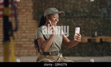 Felice soldato afro-americano che agita la mano e sorride mentre videochiama un amico o una famiglia su smartphone Foto Stock