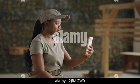 Felice soldato afro-americano che agita la mano e sorride mentre videochiama un amico o una famiglia su smartphone Foto Stock