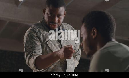 Da sotto nero militare uomo gesticulating e scolding soldato maschio su base militare Foto Stock