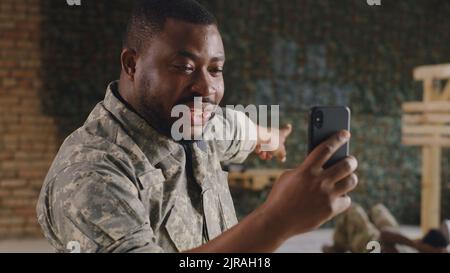 Comandante afro-americano in mimetizzazione parlando e indicando l'esercizio soldato mentre fare videochiamata in palestra della base militare degli Stati Uniti Foto Stock