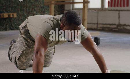 Soldato afro-americano stanco maschio in mimetizzazione fare push up e riposarsi durante l'allenamento in palestra della base militare degli Stati Uniti Foto Stock