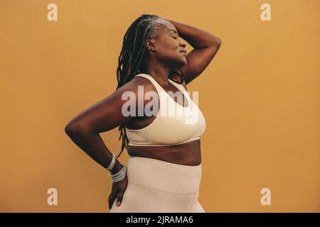 Donna atletica in piedi contro uno sfondo studio con gli occhi chiusi. Donna matura con Dreadlocks che indossa abbigliamento sportivo in uno studio. Bla sportiva Foto Stock