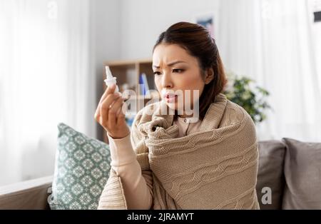 donna asiatica malata con spray nasale a casa Foto Stock