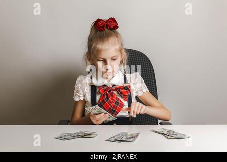 Una bambina in un uniforme della scuola sta contando i soldi - le fatture cento-dollari. Insegnare ai bambini alfabetizzazione finanziaria. Foto Stock