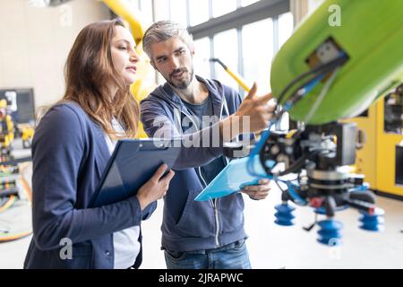 Tecnici che discutono di soluzioni tecniche relative ai robot industriali Foto Stock