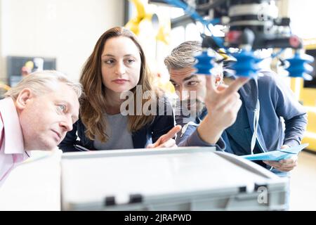 Tecnici che mostrano il nuovo robot industriale a un collega senior Foto Stock