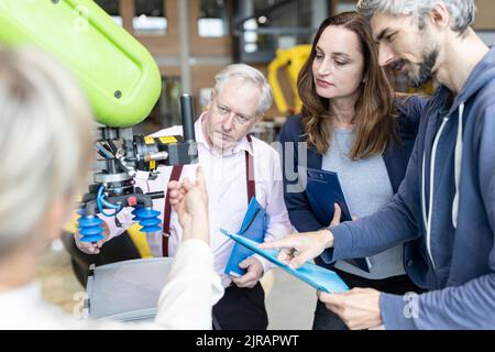 Tecnici che mostrano il nuovo robot industriale a un collega senior Foto Stock