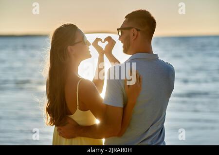 coppia felice che mostra il cuore della mano sulla spiaggia estiva Foto Stock