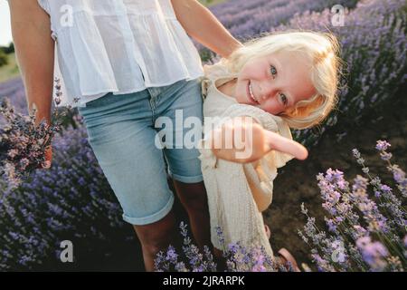 Ragazza cute felice con i capelli biondi che mostrano i pollici in piedi da madre al campo di lavanda Foto Stock