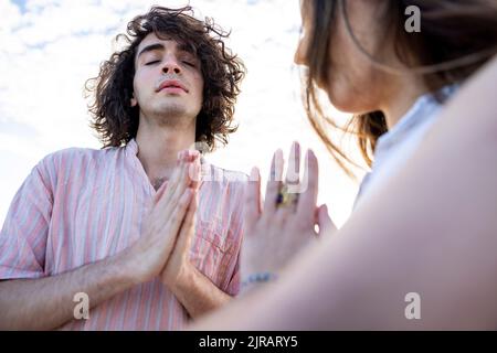 Giovane coppia che medita con le mani afferrate Foto Stock