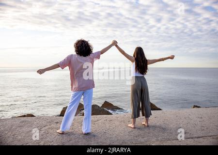 Coppia che tiene le mani in piedi con le braccia distese sul molo che guarda il mare Foto Stock