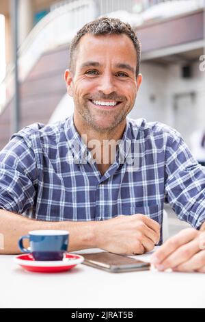 Uomo felice e maturo seduto con una tazza di caffè al tavolo al caffè all'aperto Foto Stock