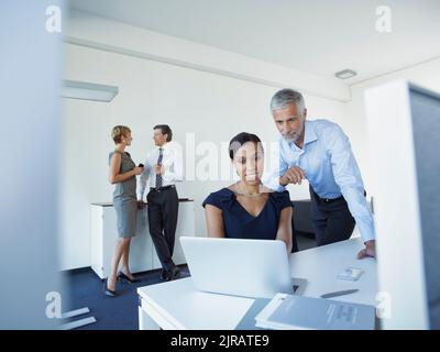 Uomo d'affari maturo e donna d'affari che usano il laptop con i colleghi che discutono in ufficio Foto Stock