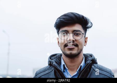 Giovane uomo sorridente con occhiali davanti al cielo Foto Stock