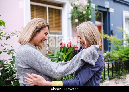 Donna felice che dà fiori a madre Foto Stock