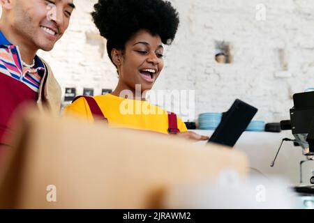 Giovane donna proprietaria con la bocca aperta utilizzando un tablet PC da un collega Foto Stock