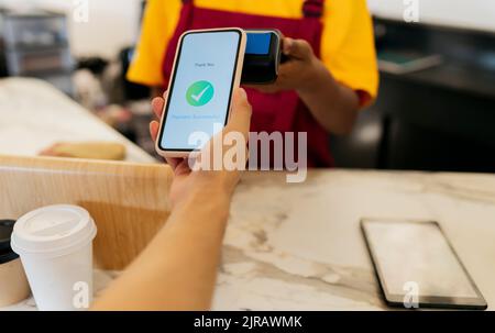 Mano del cliente che effettua il pagamento senza contatto tramite smartphone in caffetteria Foto Stock