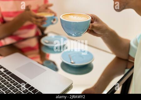 Uomo e donna che tengono tazze di cappuccino al tavolo nel caffè Foto Stock