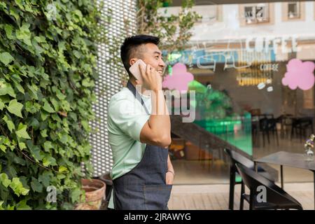 Uomo sorridente che parla sul telefono cellulare in piedi fuori dal bar Foto Stock
