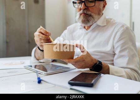 Uomo d'affari che mangia in pausa pranzo in ufficio Foto Stock