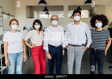 Colleghi che indossano una maschera protettiva in piedi in ufficio Foto Stock