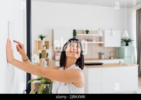 Donna che utilizza un dispositivo di automazione domestica a parete a casa Foto Stock