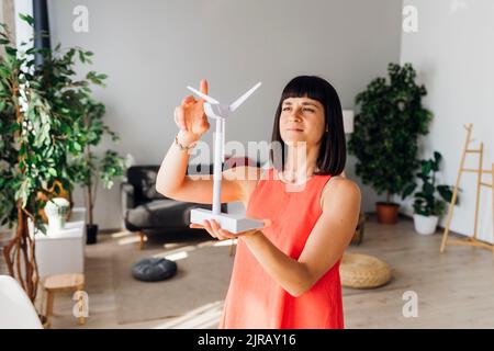 Donna che tiene il modello di turbina eolica nel soggiorno di casa Foto Stock