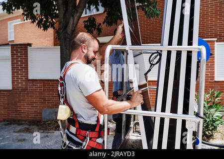 Tecnici che caricano pannelli solari in piattaforma idraulica Foto Stock