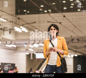 Giovane donna d'affari transgender con telefono cellulare alla stazione della metropolitana Foto Stock