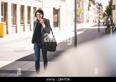 Giovane donna d'affari transgender sorridente che parla al telefono Foto Stock