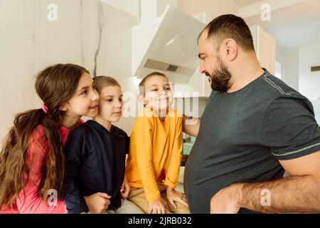 Un padre sorridente che parla con i bambini in cucina Foto Stock