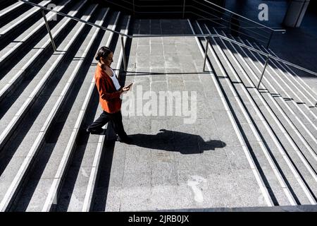 Donna d'affari che usa uno smartphone che scende sulle scale Foto Stock