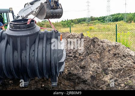 Installazione di un impianto di trattamento delle acque reflue domestiche a camera singola, l'escavatore solleva il serbatoio. Foto Stock